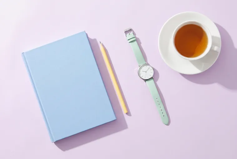 Blue notebook, pencil, wristwatch and tea on a lilac table